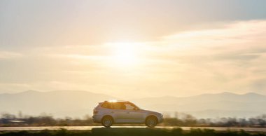 Gün batımında şehirlerarası yolda hızla giden bir SUV arabası. Akşamları otoyol trafiği.