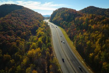 I-40 freeway road leading to Asheville in North Carolina thru Appalachian mountains with yellow fall forest and fast moving trucks and cars. Concept of high speed interstate transportation.