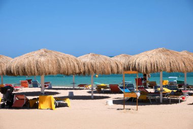 Yazın mavi renkli gökyüzüne karşı dinlenen güneşli deniz kıyılarında saman gölgesi şemsiyeleri..