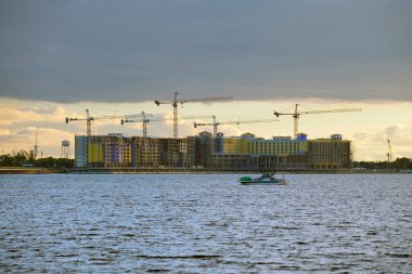 Deniz körfezi kıyısındaki inşaat alanındaki yüksek konut binalarının vinçleri ve iskelet yapısı. Rıhtımda gayrimenkul geliştirme.