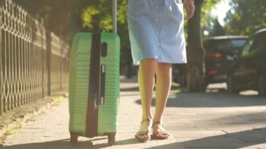 Genç bir kadının yaz günü yeşil bavuluyla kaldırımda yürümesi..