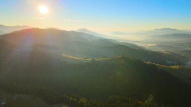 Wooded hills of Carpathian mountains in Ukraine with small traditional village houses at sunset. Brightly illuminated with setting sun evergreen woods with scattered local homes at fall season.