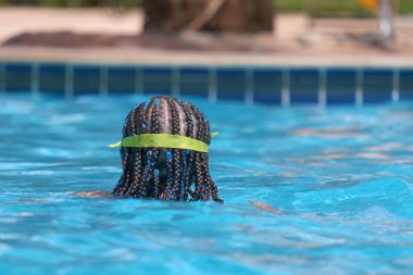 Young child girl in goggles exercises swimming in blue pool water. Summer recreation activity concept.