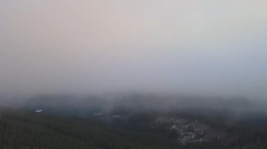 Aerial reveal shot of vibrant sunrise over white dense fog with distant dark peaks of Carpathian mountains on horizon.