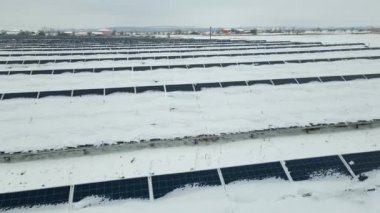 Aerial view of sustainable electrical power plant with solar photovoltaic panels covered with snow in winter for producing clean energy. Concept of low effectivity of renewable electricity in north.