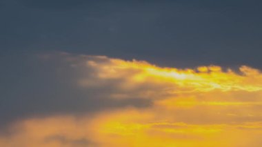 Günbatımında sarı gökyüzünde hızlı hareket eden akşam bulutlarının hızlandırılmış görüntüleri.