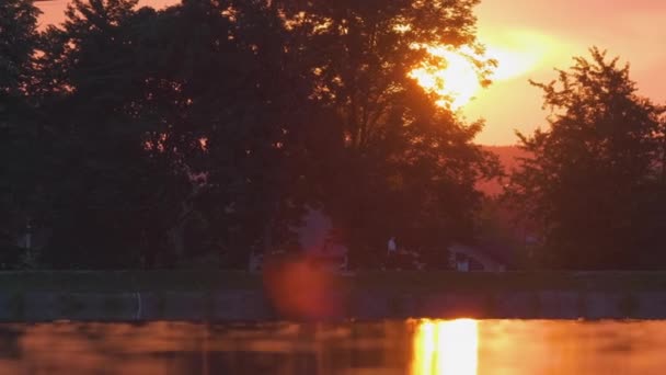 湖滨风景 湖水中映衬着深色的公园树木轮廓 夕阳西下 路堤上远行的行人 — 图库视频影像