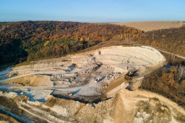 Kazı araçları ve çöp kamyonlarıyla inşaat endüstrisi için kireçtaşı malzemelerinin açık maden sahasının hava görüntüsü.