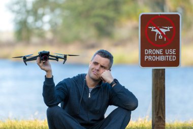 Drone operator is disappointed because he isnt allowed to fly his quadcopter in national park no drone area. Man is unable to use his UAV near restriction notice sign. Airspace use regulations.