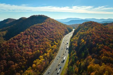 I-40 freeway road leading to Asheville in North Carolina over Appalachian mountain pass with yellow fall forest and fast moving trucks and cars. Concept of high speed interstate transportation.
