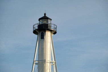 White tall lighthouse on sea shore against blue sky for commercial vessels navigation.