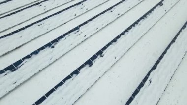 Aerial view of sustainable electrical power plant with solar photovoltaic panels covered with snow in winter for producing clean energy. Concept of low effectivity of renewable electricity in north.