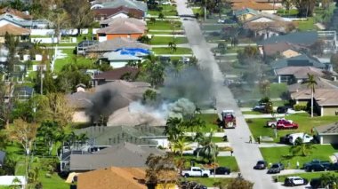 View from above of burning private house on fire and firefighters extinguishing flames after short circuit caused to ignite roof damaged by hurricane Ian wind. Home disaster in Florida suburban area.