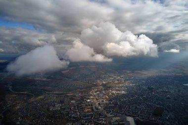 Uzak şehrin yüksek irtifasındaki uçak penceresinden hava manzarası beyaz kabarık kümülüs bulutlarıyla kaplı..