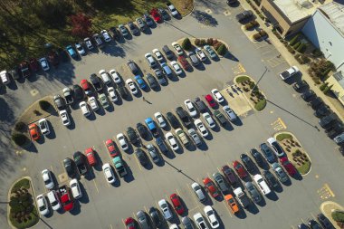 Aerial view of large parking lot with many parked colorful cars. Carpark at supercenter shopping mall with lines and markings for vehicle places and directions.