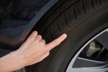 Kadın sürücü elleri yeni arabasının tekerlek lastiklerini inceliyor. Araç güvenliği kavramı.