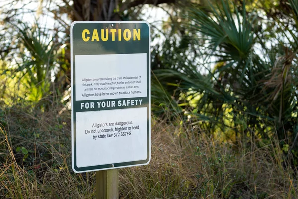 Alligators warning sign in Florida state park about caution and safety during trail walk.
