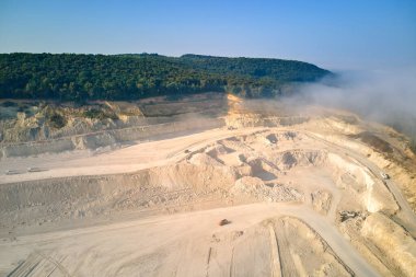 Kazı araçları ve çöp kamyonları ile inşaat endüstrisi için kireçtaşı malzemelerinin açık çukur madenciliğinin hava görüntüsü.