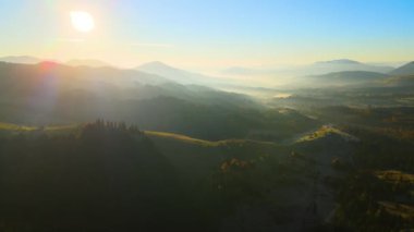 Aerial view of Carpathian mountain hills with small ukrainian village houses at sunset. Brightly illuminated pine woods with scattered local settlement homes at fall season.