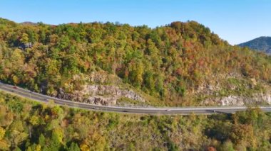 View from above of national freeway route in North Carolina leading thru Appalachian mountains with yellow fall woods and fast moving trucks and cars. Interstate transportation concept.