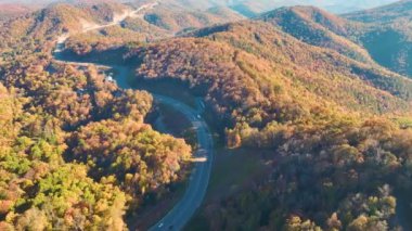 High point of view of highway route in North Carolina through Appalachian mountains in golden fall season with fast moving trucks and cars. Interstate transportation concept.