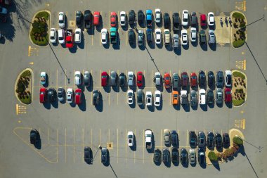 Aerial view of many colorful cars parked on parking lot with lines and markings for parking places and directions. Place for vehicles in front of a strip mall plaza.