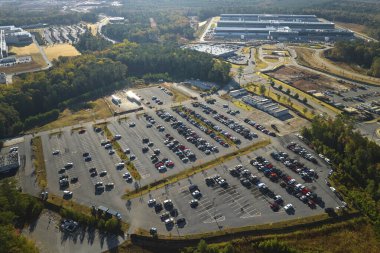 Aerial view of many employee cars parked on parking lot in front of industrial factory building.