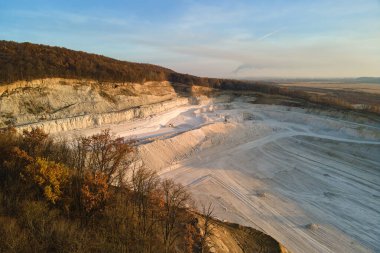 Kazı makineleri ve çöp kamyonlarıyla inşaat endüstrisi için kumtaşı malzemelerinden oluşan açık maden manzarası. Madencilik ve kullanışlı mineral üretiminde ağır ekipman.