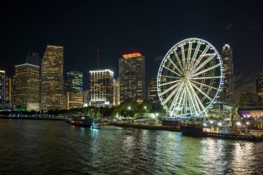 Aerial view of Skyviews Miami Observation Wheel at Bayside Marketplace with reflections in Biscayne Bay water and high illuminated skyscrapers of Brickell, citys financial center at night.