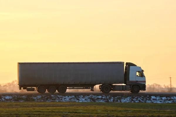 Semi-truck with cargo trailer driving on highway hauling goods in evening. Delivery transportation and logistics concept.