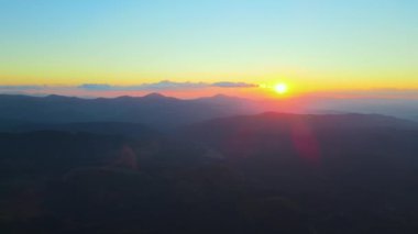 Gün batımında gün batımında parlak güneş ışınlarıyla karanlık dağ tepelerinin havadan görünüşü. Akşamları sisli tepeler ve sisli vadiler.