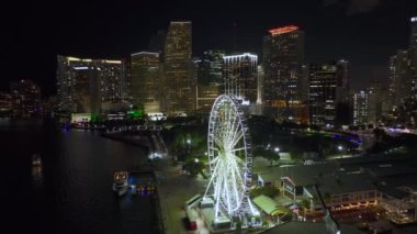 Aerial view of Skyviews Miami Observation Wheel at Bayside Marketplace with reflections in Biscayne Bay water and high illuminated skyscrapers of Brickell, citys financial center at night.