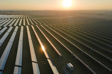 Günbatımında temiz elektrik enerjisi üretmek için birçok sıra güneş fotovoltaik paneli bulunan sürdürülebilir büyük elektrik santralinin havadan görünüşü. Sıfır emisyon kavramı ile yenilenebilir elektrik.