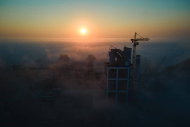 Beton yapılı çimento fabrikasının havadan görünüşü ve sisli bir akşamda endüstriyel üretim alanında kule vinci. Üretim ve küresel sanayi kavramı.