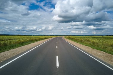 Yeşil tarım alanları arasındaki boş şehirlerarası yolun havadan görünüşü. Karayolu insansız hava aracının üst görüntüsü.