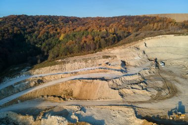 Kazı araçları ve çöp kamyonlarıyla inşaat endüstrisi için kireçtaşı malzemelerinin açık maden sahasının hava görüntüsü.