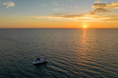 Tanımlanamayan insanların gün batımında beyaz yatta yüzen dalgalı deniz dalgaları üzerinde eğlendikleri hava manzarası. Okyanus yüzeyinde motorlu tekne tatili.