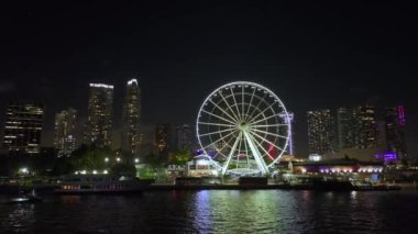 Aerial view of Skyviews Miami Observation Wheel at Bayside Marketplace with reflections in Biscayne Bay water and high illuminated skyscrapers of Brickell, citys financial center at night.