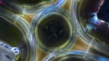 Şehir caddesinin kavşağındaki trafiğin en üst görüntüsü gece hızlı hareket eden arabalarla. Aydınlatılmış kentsel dairesel ulaşım kavşağının zamanlaması.