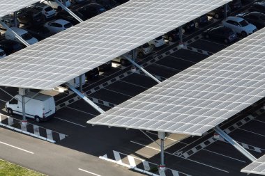 Güneş panellerinin hava görüntüsü park yerinin üzerine gölge çatısı olarak yerleştirilmiş ve temiz elektriğin etkin üretimi için park edilmiş arabalar var. Fotovoltaik teknoloji şehir altyapısına entegre edildi.