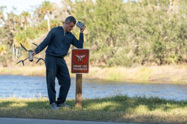 Drone operator is disappointed because he isnt allowed to fly his quadcopter in national park no drone area. Man is unable to use his UAV near restriction notice sign. Airspace use regulations.