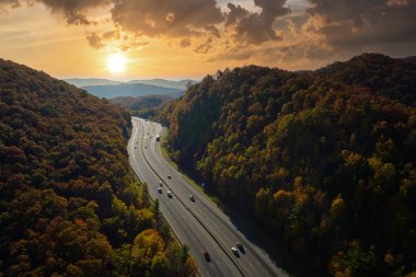I-40 freeway road leading to Asheville in North Carolina thru Appalachian mountains with yellow fall forest and fast moving trucks and cars. Concept of high speed interstate transportation.
