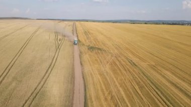 Tarım buğday tarlaları arasında toprak yolda giden kargo kamyonunun hava görüntüsü çok toz yapıyor. Hasat mevsiminde hasatçıların topladığı tahıl naklinden sonra..