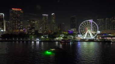Aerial view of Skyviews Miami Observation Wheel at Bayside Marketplace with reflections in Biscayne Bay water and high illuminated skyscrapers of Brickell, citys financial center at night.