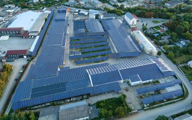 Sanayi binasının çatısına yeşil ekolojik elektrik üretmek için monte edilmiş mavi fotovoltaik panelli güneş enerjisi santralinin hava görüntüsü. Sürdürülebilir enerji konsepti üretimi.