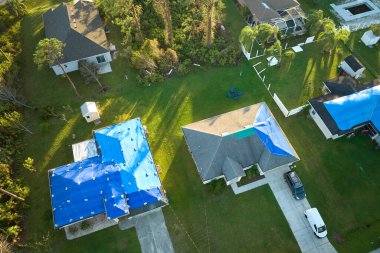 Asfalt kiremitlerin yerine konana kadar yağmur suyu sızıntılarına karşı koruyucu branda örtüleriyle kaplı çatı sızdıran evin üst görüntüsü. Florida 'daki Ian Kasırgası' nın yol açtığı çatı hasarı.