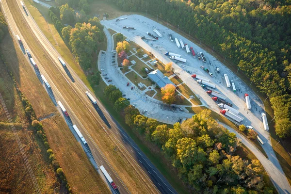 View from above of big parking rest area for cars and trucks near busy american highway with fast moving traffic. Recreational place during interstate travel.