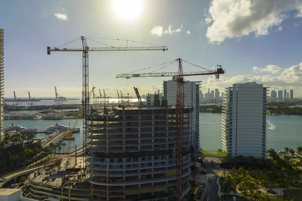 Tower lifting cranes at high residential apartment building construction site. Real estate development in Miami urban area.