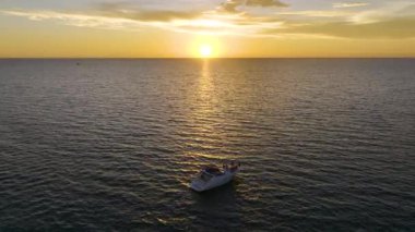 Tanımlanamayan insanların gün batımında beyaz yatta yüzen dalgalı deniz dalgaları üzerinde eğlendikleri hava manzarası. Okyanus yüzeyinde motorlu tekne tatili.