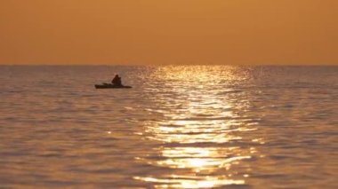 Sporcunun karanlık figürü gün batımında deniz suyunda kano teknesinde tek başına kürek çekiyor. Aktif ekstrem spor konsepti.